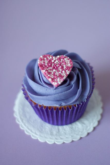 Purple cupcake featuring heart shaped sprinkle decoration on top of smooth frosting. Ideal for Valentine's Day promotions, dessert recipes, bakery marketing materials, festive celebrations, and elegant parties.