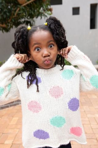 Playful girl in polka-dot sweater making funny faces outdoors