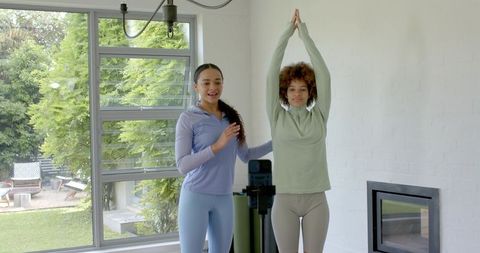 Yoga instructor guiding client raising arms in bright home studio with tripod and foam roller