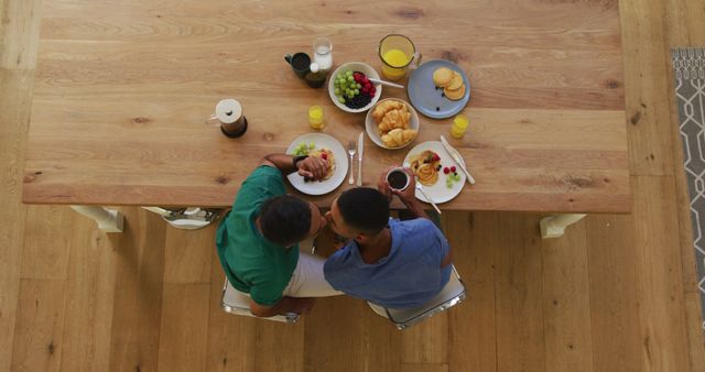 Overhead view of biracial gay male couple having breakfast at table. staying at home in isolation during quarantine lockdown.