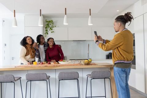 African american family laughing at kitchen island while man uses smartphone