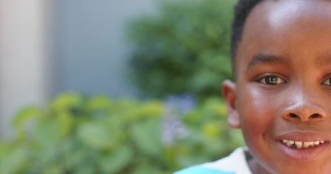 African school-age boy smiling, looking at camera closeup wearing striped shirt with garden bokeh
