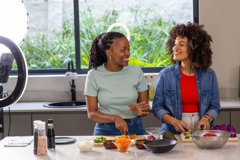 Diverse friends chopping vegetables while filming cooking tutorial in modern kitchen studio