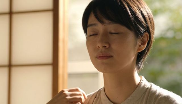 Asian woman practicing mindful breathing, eyes closed touching shoulder near shoji screen