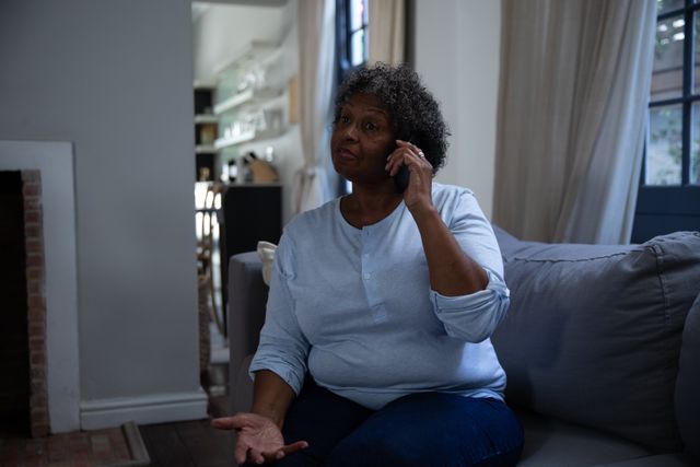 African American senior woman talking on the phone, sitting on a couch, in the living room at home. Domestic life and older people using technology. 