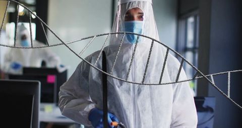 Lab Technician Wearing Full PPE Inspecting Sample with DNA Helix Overlay in Laboratory