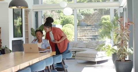 African american mother guiding daughter on laptop in bright modern open-plan living area