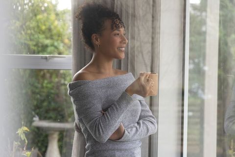 African american woman enjoying morning coffee by window in cozy gray sweater