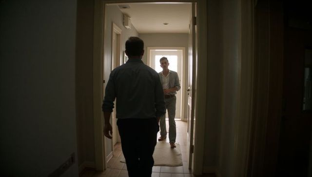 Two men walking toward backlit glass door in home hallway wearing casual business attire