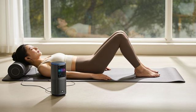 Asian woman resting on yoga mat using foam roller and smart speaker for guided recovery
