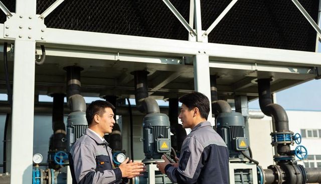 Two technicians discussing pump motors at industrial plant with blue valves and piping