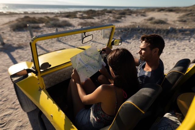 Couple sitting in a yellow beach buggy on a sunny beach, looking at a map and discussing their route. Ideal for use in travel blogs, vacation planning websites, adventure tourism promotions, and romantic getaway advertisements.
