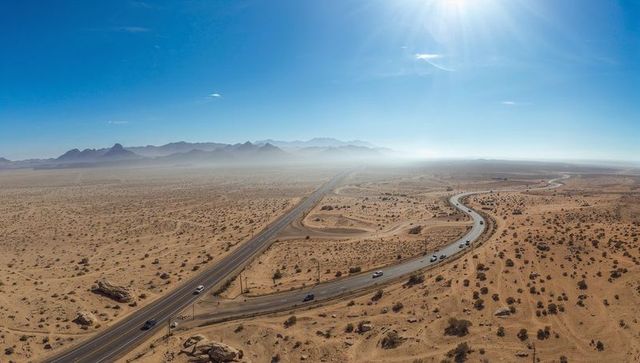 Aerial highway curves cutting across sunlit desert plain with cars, ramps and distant mountains
