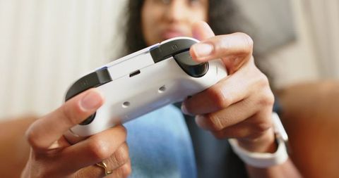 African american woman playing video games with white wireless controller on cozy couch