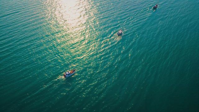 Aerial trio of motorboats cruising turquoise sea with sunlit wake trails