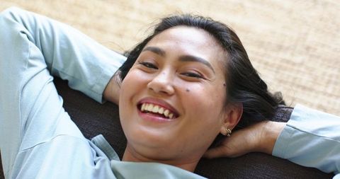 Asian woman relaxing on sofa smiling close-up, casual home lifestyle and self-care