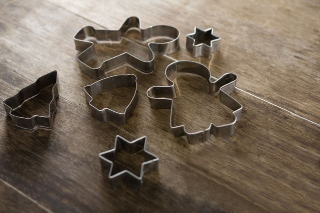Various metal cookie cutters in different shapes, including gingerbread men, stars, and trees, are scattered on a wooden table. Ideal for use in holiday baking promotions, kitchenware advertisements, or cooking blogs.