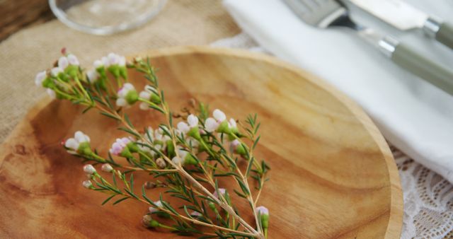 This image captures a rustic wooden plate with a blooming flower twig strategically placed on a casual table setup. The ambiance emphasizes the natural, raw aesthetic typical of rustic dining themes. This image can be used for promoting home decor inspiration, culinary presentations, or nature-inspired design concepts.