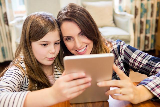 Mother and daughter using digital tablet in living room at home, sharing quality time. Ideal for educational content, family technology use, and parenting articles.