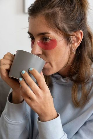 Sipping morning coffee while wearing under-eye patches and hoodie, cozy self-care closeup