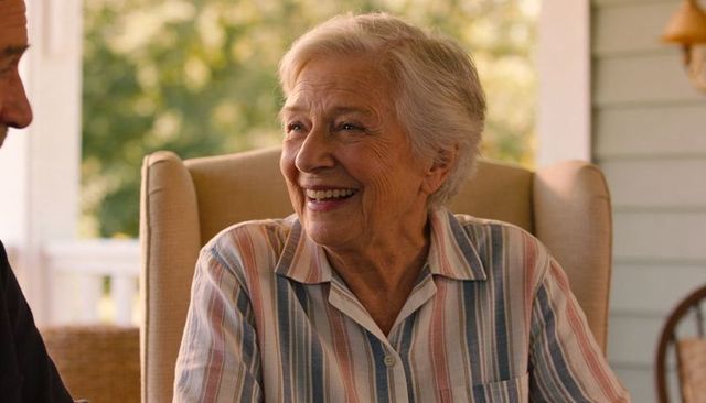 Smiling senior woman sitting on sunlit porch in pastel striped shirt