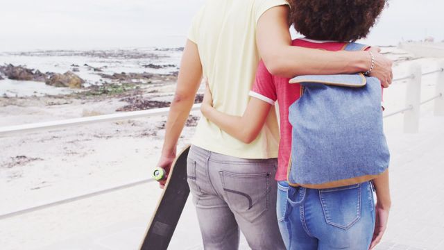 Young African American couple enjoying leisure time while walking on beach promenade, reinforcing love and connection. Perfect for use in advertisements and campaigns promoting tourism, outdoor activities, youth culture, relationships, and casual lifestyle.