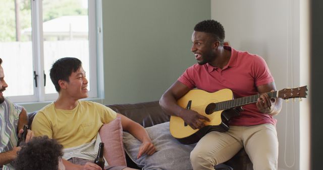 Happy diverse male friends playing guitar and talking in living room. spending quality time at home together.