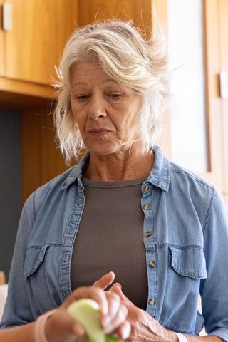 Senior woman peeling green fruit in sunlit kitchen, candid home cooking portrait, healthy aging