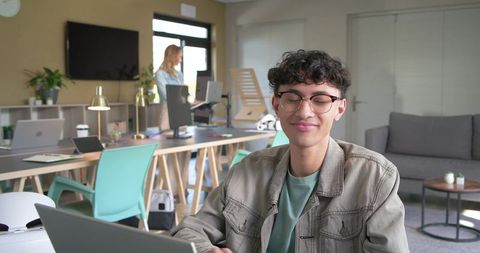 Young professional smiling while working on laptop in sunlit modern coworking space