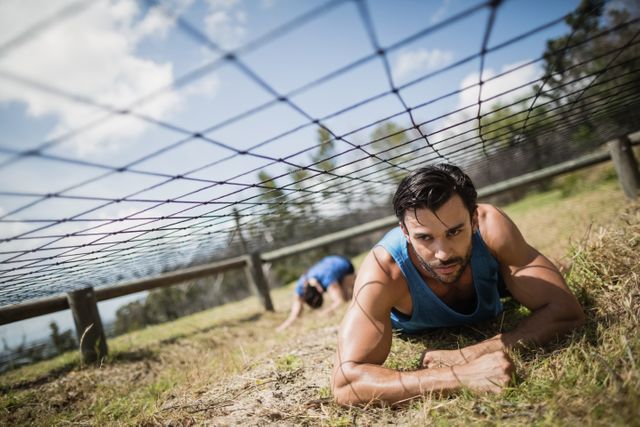 Fit man crawling under the net during obstacle course in boot camp