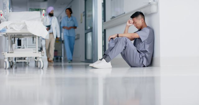 Exhausted asian male surgeon leaning on wall in hospital corridor. Medicine, despair, healthcare and hospital, unaltered.