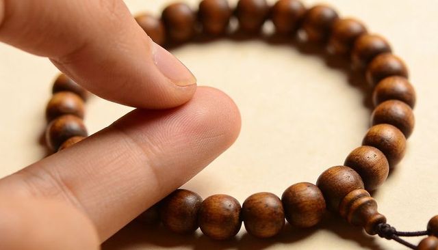 Fingertips touching polished wooden prayer beads showing wood grain and texture