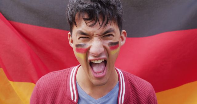 Young man with face painted in Germany flag colors, expressing excitement and enthusiasm. Suitable for themes of sports events, fan celebrations, promoting national pride, and patriotic campaigns.