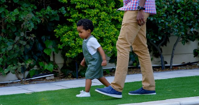 Shows a father and child spending quality time walking in a garden surrounded by greenery. This image could be used in articles or advertising related to family activities, parenting tips, outdoor hobbies, and lifestyle content emphasizing nature and familial bonds.