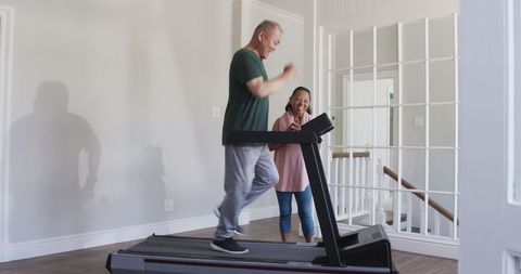 Senior man jogging on treadmill with supportive young girl