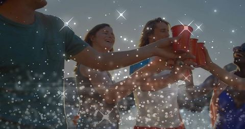 Friends clinking red cups at sunset beach party celebrating summer together