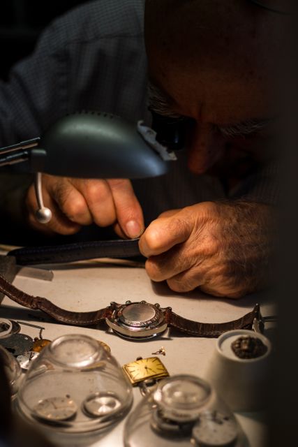 Close-up of an experienced watchmaker repairing a vintage watch. His hands meticulously working with delicate tools, reflecting the high skill and precision required in horology. This image is perfect for illustrating craftsmanship, traditional skills, and the intricacies of watchmaking. It can be used in articles, blog posts, and advertisements related to watch repair, manual labor, and craftsmanship.