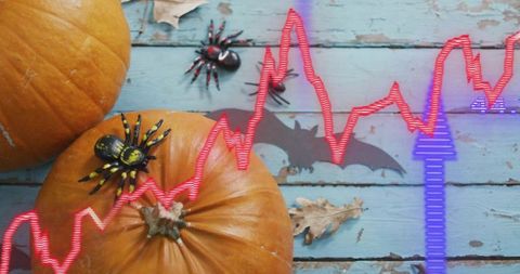 Halloween pumpkins with toy spiders and neon stock chart overlay on weathered blue wood