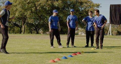 Youth sports team practicing agility drill on sunny grass field with colored cones