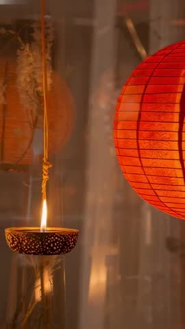 Vertical video showing flickering oil lamp and glowing red paper lantern reflecting on glass