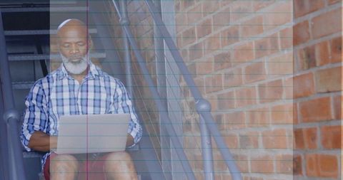Man in Plaid Shirt Working on Laptop in Urban Stairwell