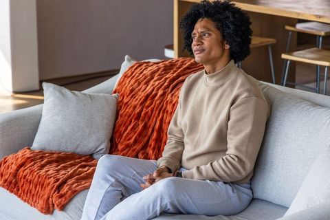 African american man sitting on gray sofa looking thoughtful in cozy modern living room