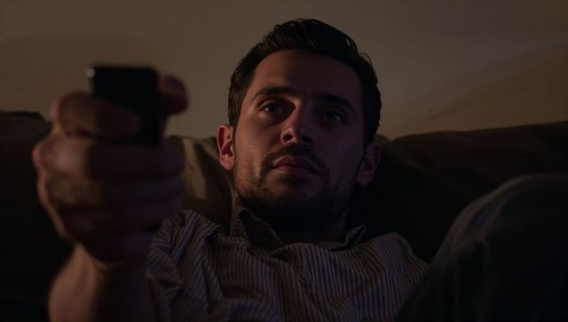 Reclining man holding remote control in warm evening light on sofa, intimate home moment