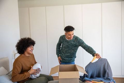 Joyful Male Roommates Unpacking Clothes in Bedroom