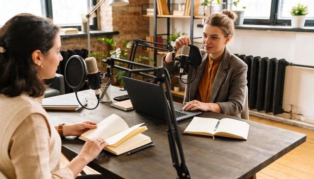 Recording collaborative podcast interview with two women hosts adjusting microphones in studio