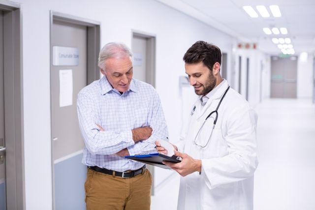 Doctor discussing medical report with senior patient in hospital corridor. Ideal for healthcare, medical consultation, patient care, and hospital-related content. Useful for illustrating doctor-patient interactions, medical advice, and healthcare services.