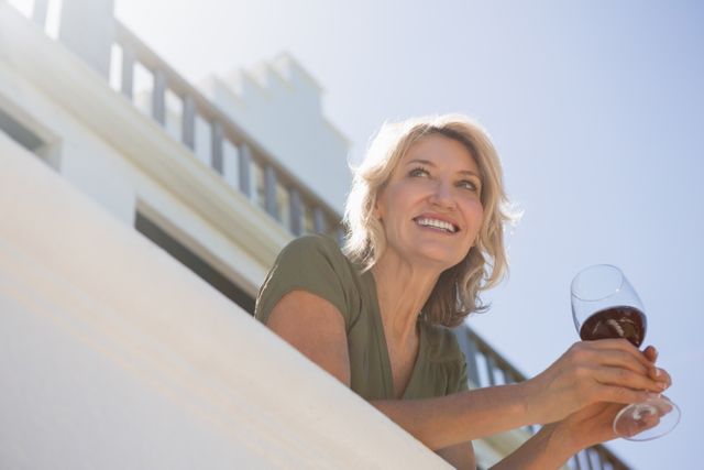 Low angle view of cheerful woman holding red wine glass in balcony at restaurant
