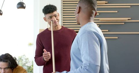 Multicultural young men socializing while holding pool cues in modern lounge with plants