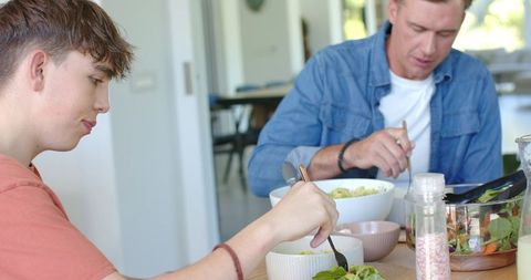 Father and teenage son sharing healthy salad at dining table during casual family mealtime