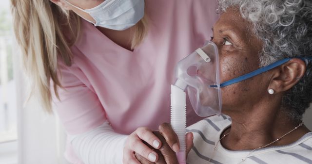 A nurse is helping an elderly woman by adjusting her oxygen mask. The nurse is wearing a mask and a pink uniform. This image can be used to depict healthcare services, elderly care, compassionate caregiving, medical assistance, and respiratory treatments. It is suitable for use in hospital promotions, healthcare facilities, caregiving articles, and medical education resources.